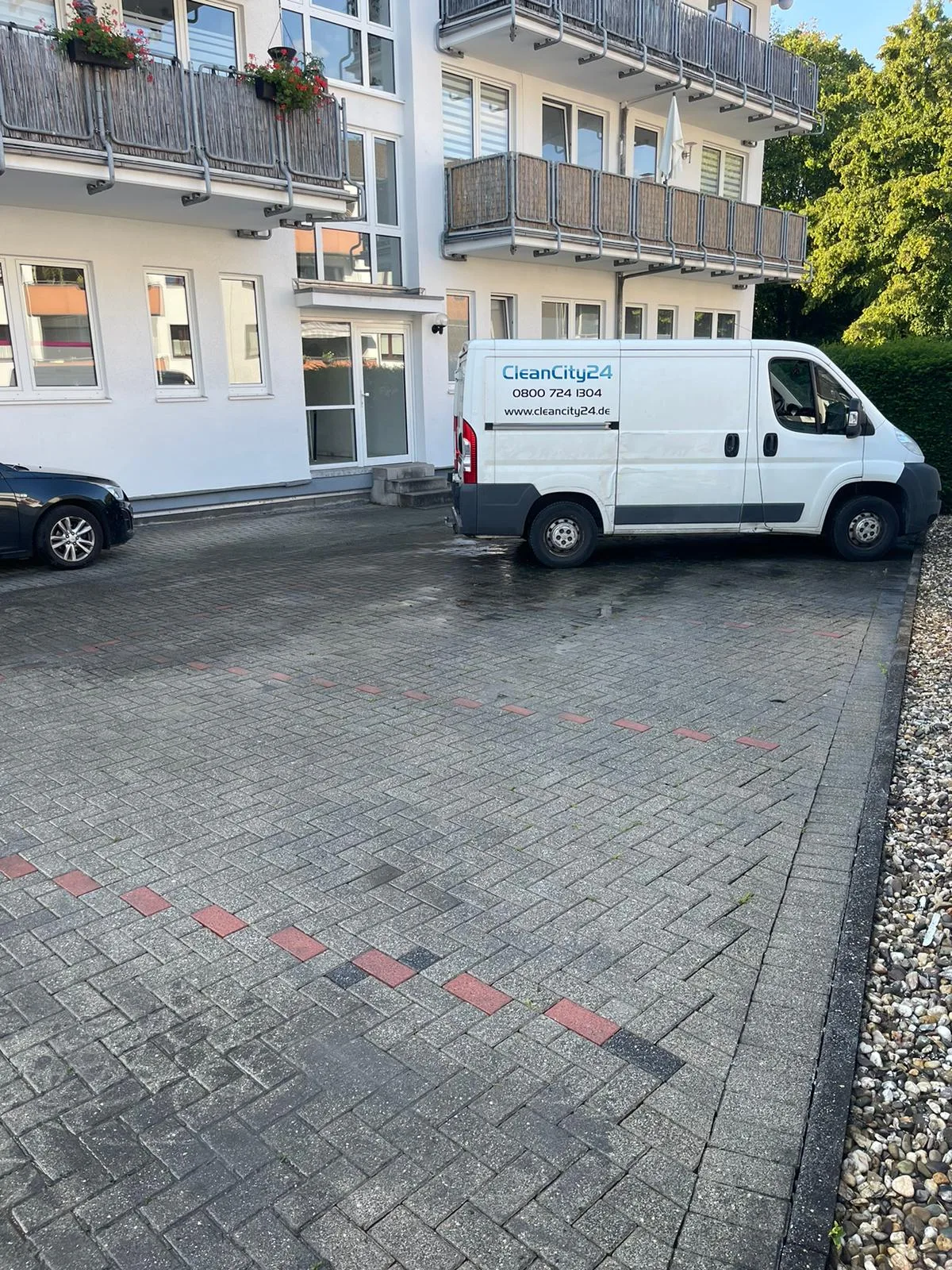Mycie kostki brukowej przed budynkiem z zaparkowanymi samochodami